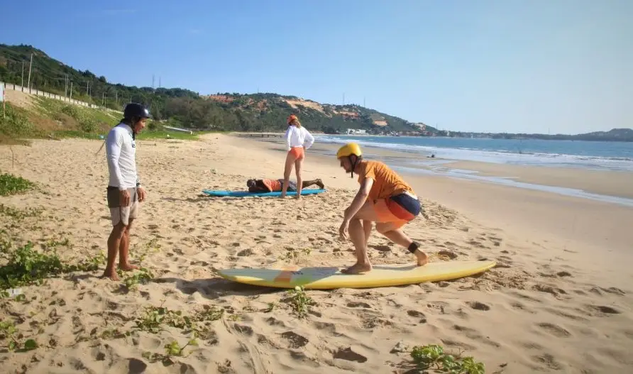 A surf coach and a student practising on a surfboard on the sand of a beach in Mui Ne