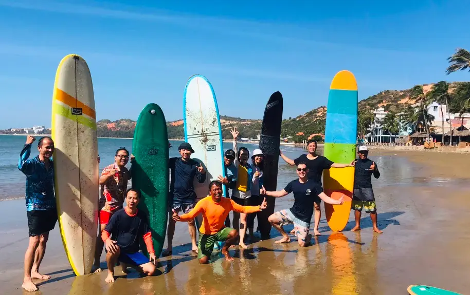 The UW Kite Surf team and guests posing on the beach in Mui Ne with a row of surfboards