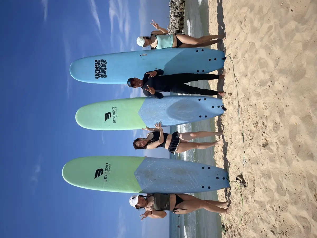 A Vietnam Surftrip coach and three students standing with their surfboards on the beach after a lesson