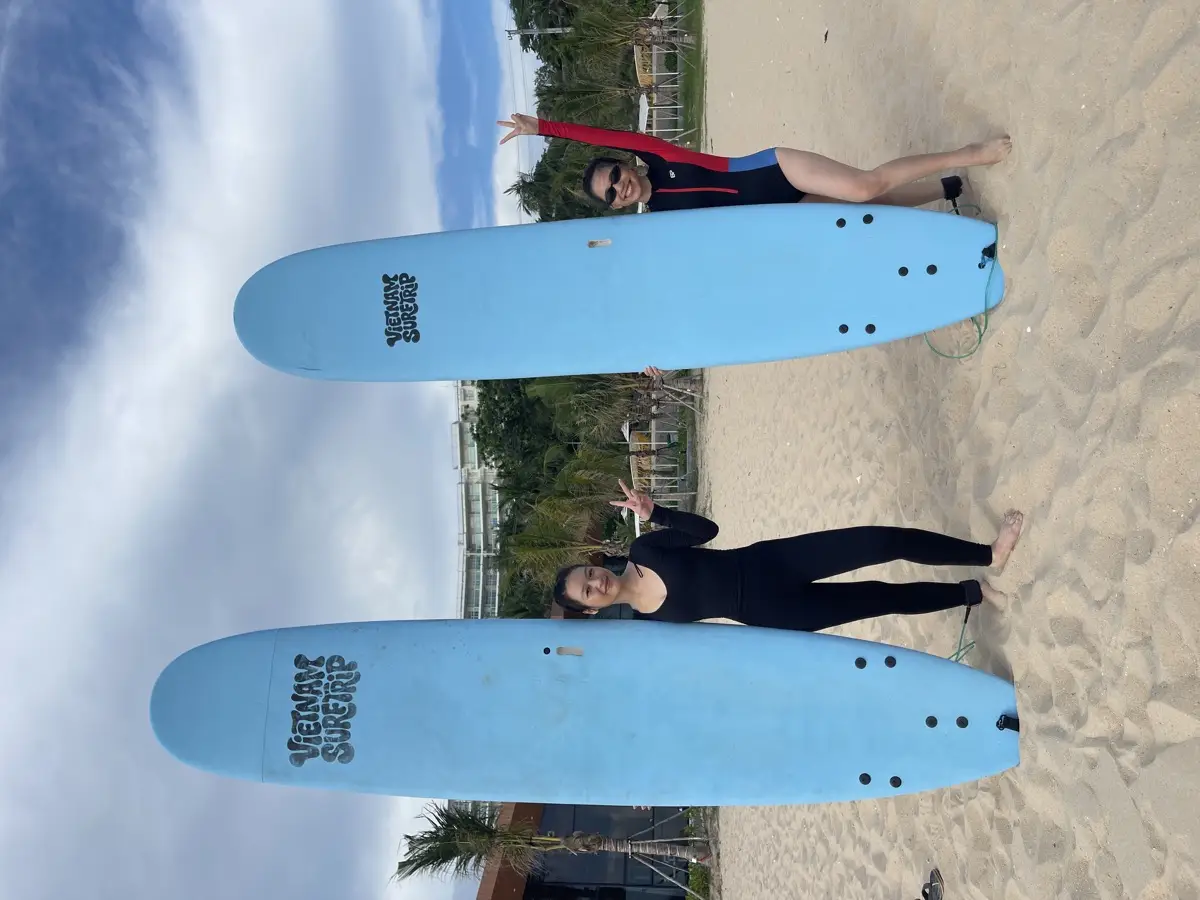 Two students in wetsuits standing next to Vietnam Surftrip soft-top surfboards on the beach